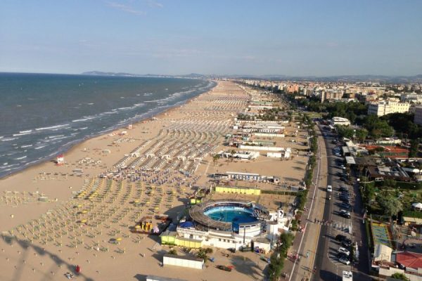 Spiaggia affollata con ombrelloni e veduta della costa di una città balneare.