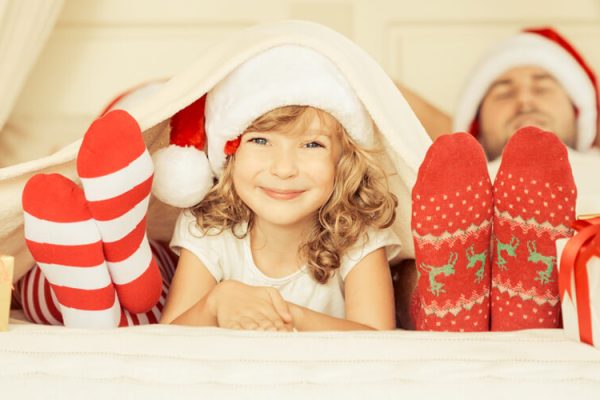Bambina sorridente con cappello di Natale tra due persone distese con calzini natalizi.
